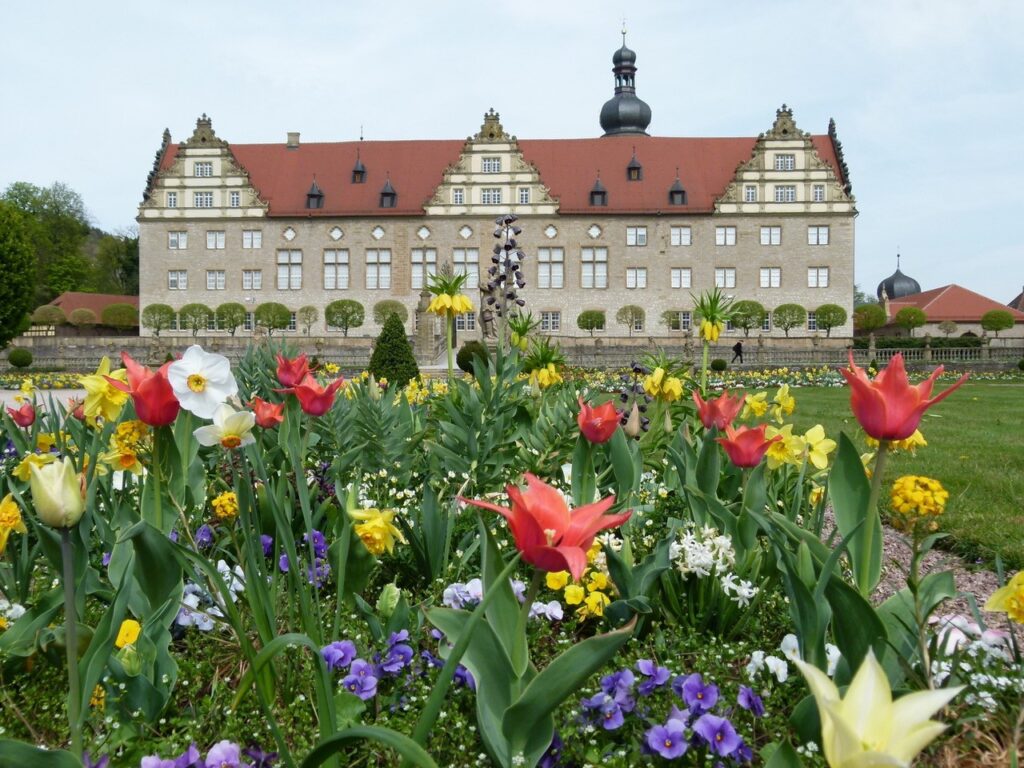 Bunte Blumenpracht vor einem barocken Schloss mit Turm und rotem Ziegeldach
