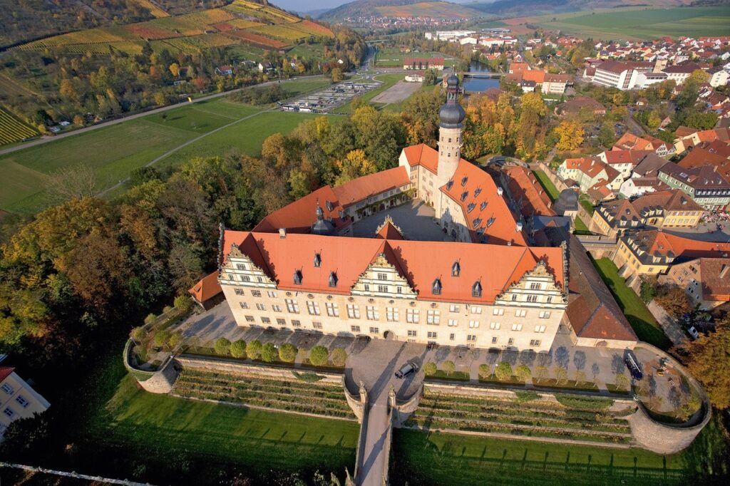 Ein prächtiges, barockes Schloss mit rotem Dach aus der Luft betrachtet