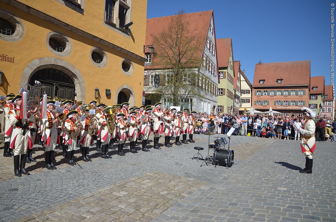 Eine uniformierte Musikkapelle spielt vor Publikum auf einem mittelalterlichen Stadtplatz