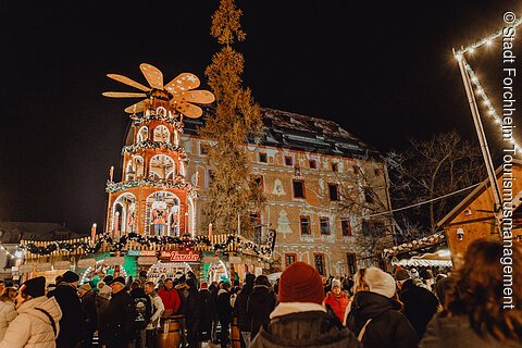 Eine Weihnachtspyramide sticht aus einem bunt beleuchteten Weihnachtsmarkt heraus.
