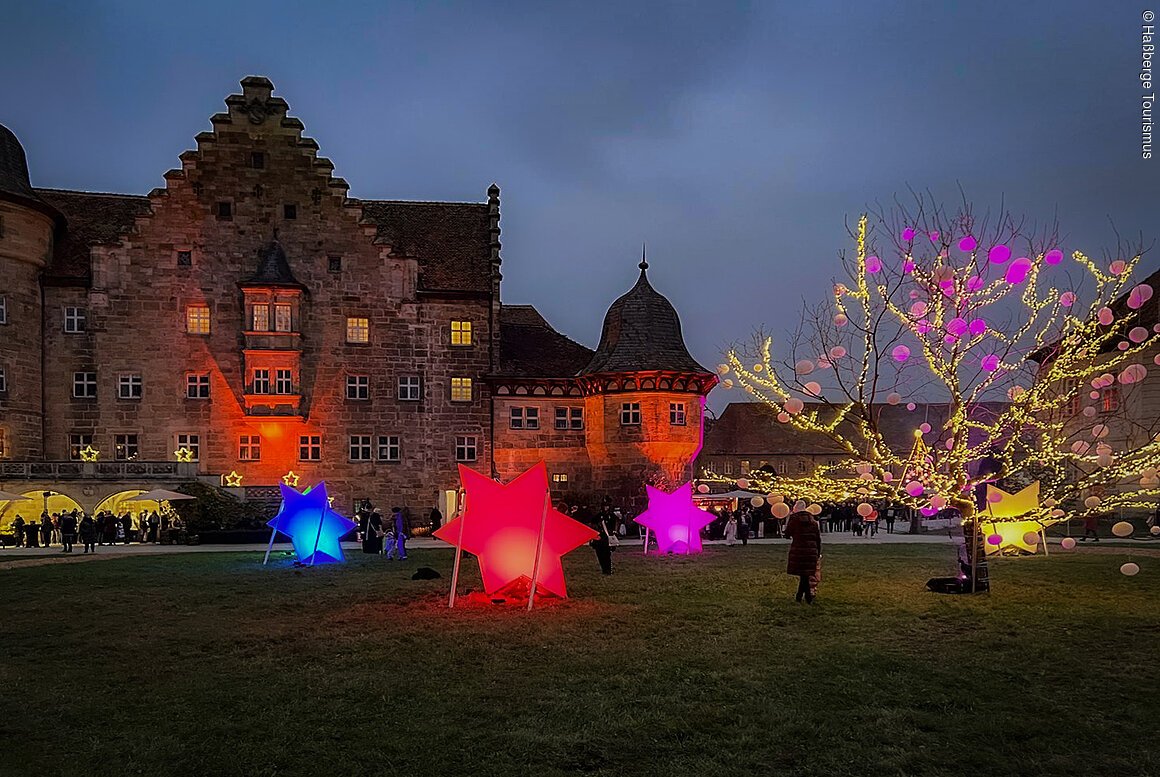 Weihnachtsland Franken (Königsberg i.Bay. / Haßberge) Ein historisches Gebäude bei Nacht mit beleuchteten Lampions und einem Baum mit Lichterketten im Vordergrund.