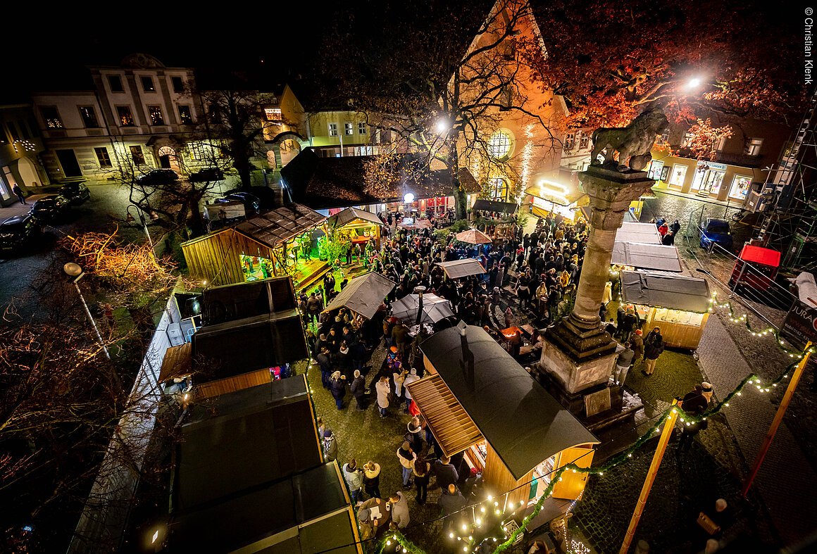 Vogelperspektive auf einen belebten Weihnachtsmarkt bei Nacht mit Ständen und Menschen.