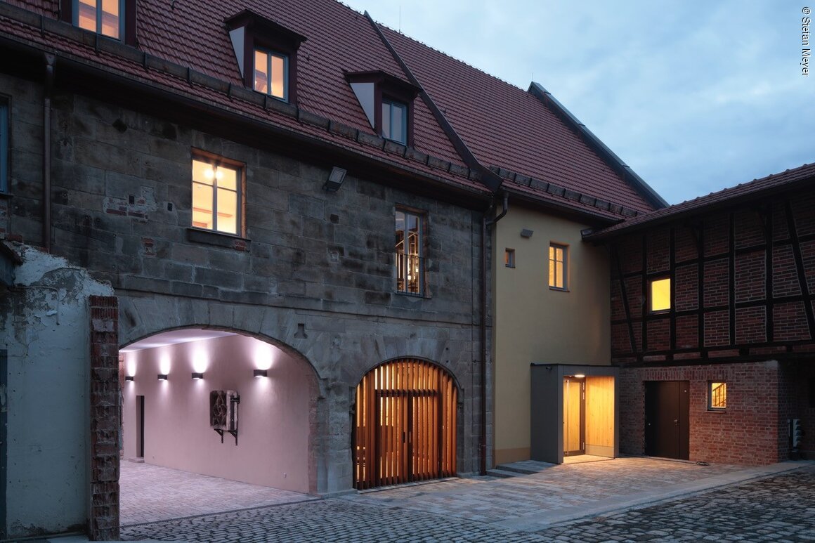 Bildungs- und Kulturscheune (Langenzenn, Romantisches Franken) Beleuchteter Innenhof mit renoviertem Gebäude, Fachwerk und gepflastertem Boden.