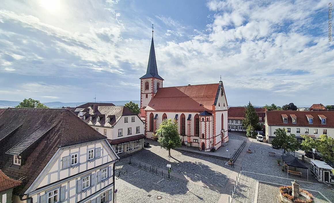 Stadtpfarrkirche (Hofheim i.UFr., Haßberge) Historisches Gebäude mit Kirchturm auf einem gepflasterten Platz, umgeben von Fachwerkhäusern.