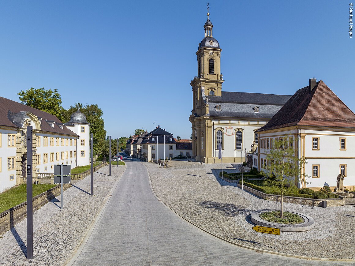 Pflasterstraße mit historischen Gebäuden und einer Kirche im Hintergrund bei klarem Himmel.