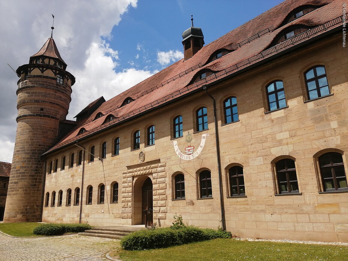Festung (Lichtenau, Romantisches Franken) Historisches Gebäude mit Turm und Sonnenuhr, blauer Himmel und Wolken im Hintergrund.