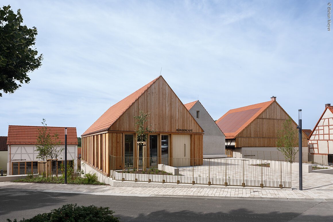 Bürgercafe (Niederwerrn, Fränkisches Weinland) Mehrere moderne Gebäude mit Satteldächern und Holzverkleidung, darunter ein Bürgercafé.