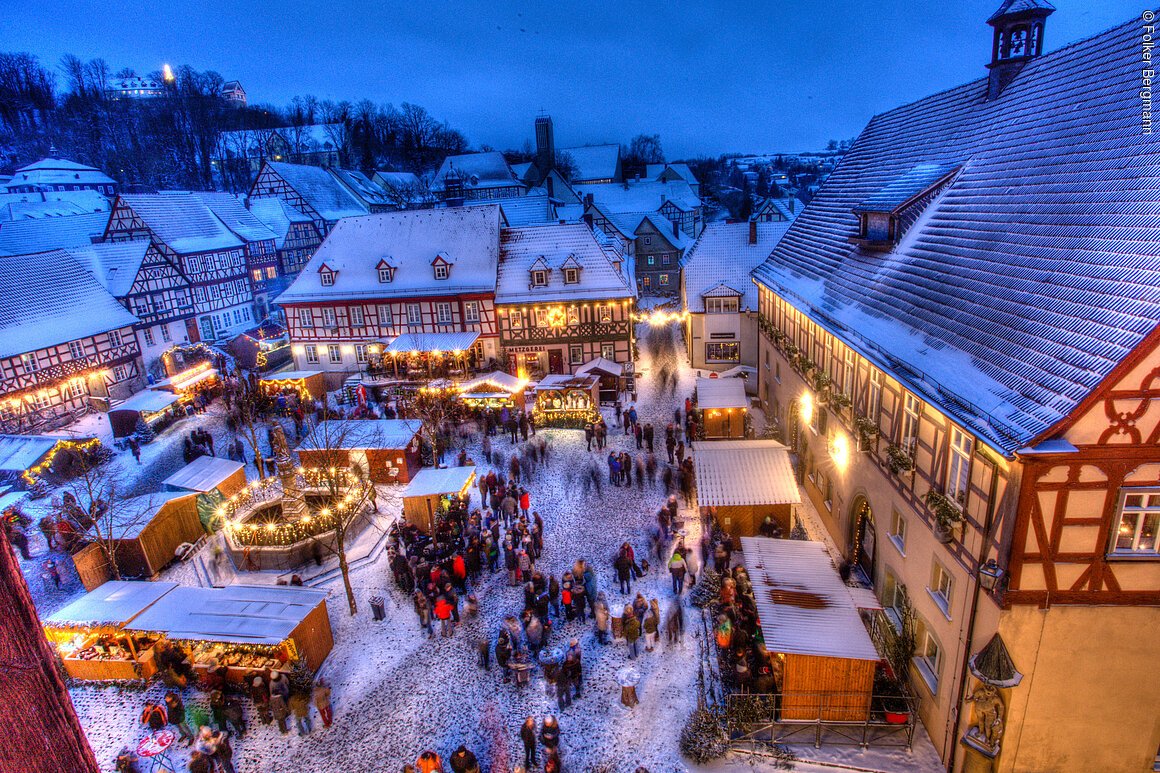 Verschneiter Weihnachtsmarkt in einem historischen Dorf mit Fachwerkhäusern und festlich beleuchteten Ständen.