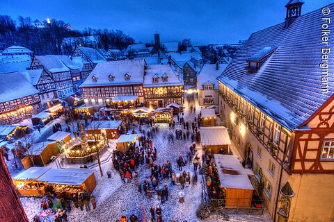 Verschneiter Weihnachtsmarkt in einem historischen Dorf mit Fachwerkhäusern und festlich beleuchteten Ständen.