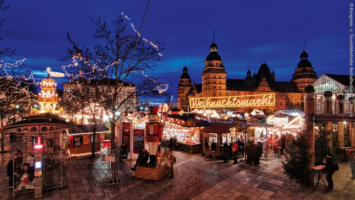 Weihnachtsmarkt mit Lichtern und Menschen, im Hintergrund ein historisches Gebäude bei Nacht.
