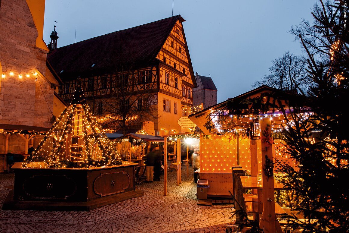 Weihnachten in Dinkelsbühl (Dinkelsbühl, Romantisches Franken) Weihnachtsmarkt mit beleuchteten Ständen und Fachwerkhaus im Hintergrund bei Dämmerung.