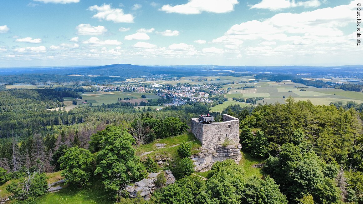 Burgruine Epprechtstein (Kirchenlamitz, Fichtelgebirge) Luftaufnahme einer Burgruine auf einem bewaldeten Hügel mit Blick auf eine ländliche Landschaft und eine Stadt.