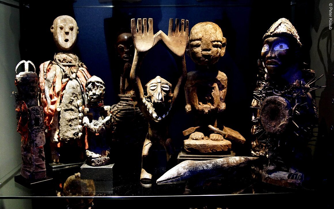 Verschiedene traditionelle Holzskulpturen und Figuren in einem Ausstellungsraum.