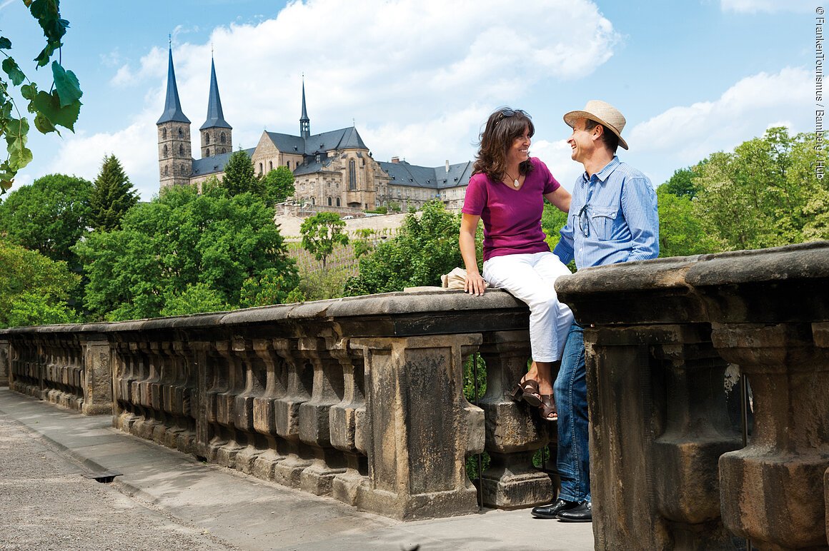 Ein Paar sitzt auf einer Steinbalustrade mit Blick auf eine historische Kirche im Hintergrund.