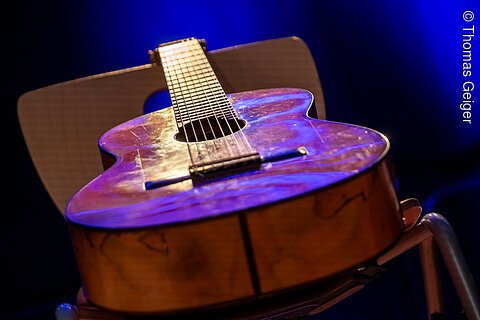 Akustische Gitarre liegt auf einem Stuhl vor blauem Hintergrund, Nahaufnahme vom Korpus und Hals