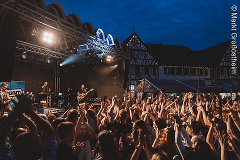 Menschenmenge bei Nacht vor Bühne mit Live-Band und Fachwerkhäusern im Hintergrund