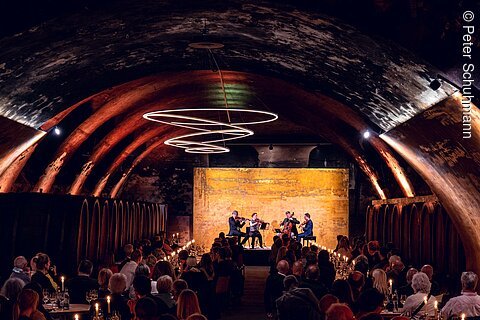 Konzert mit Streichquartett in einem Gewölbekeller mit Publikum und Kerzenlicht an langen Tischen.