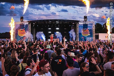 Große Menschenmenge vor Bühne mit Sängerin und Flammen bei Mallorca Sommer Festival im Freien.