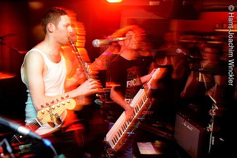 Musiker spielen Klarinette und Keytar auf Bühne mit roter Beleuchtung und verschwommenen Bewegungen.
