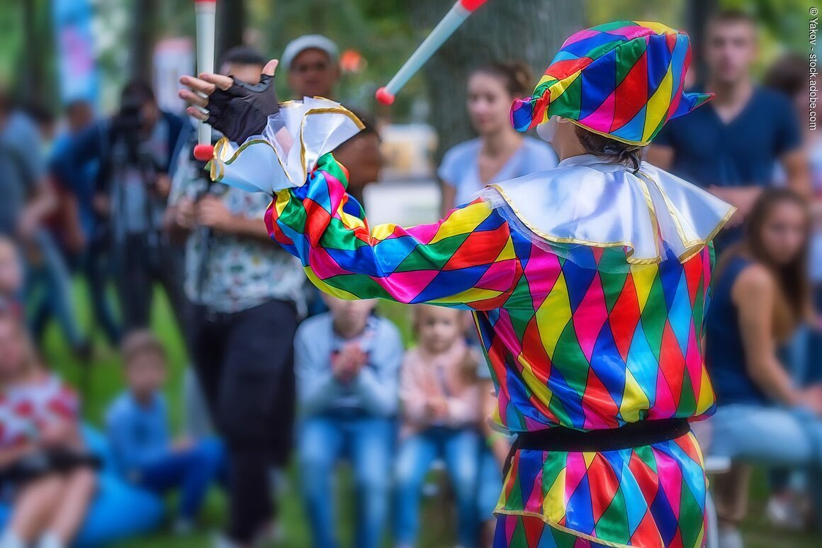Back view of a street harlequin in colorful costume juggling in the street